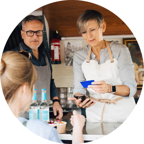 A bar server holds a credit card and smart phone for a tap to pay transaction while another server and the customer look on.