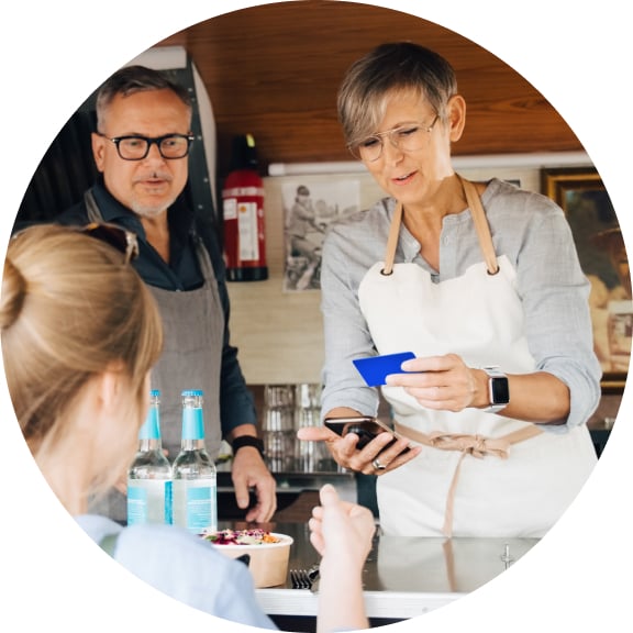 A bar server holds a credit card and smart phone for a tap to pay transaction while another server and the customer look on.