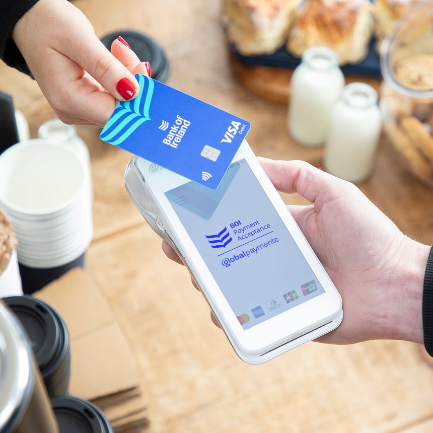 A customer taps a Bank of Ireland Visa card against a mobile card machine to make a contactless payment.